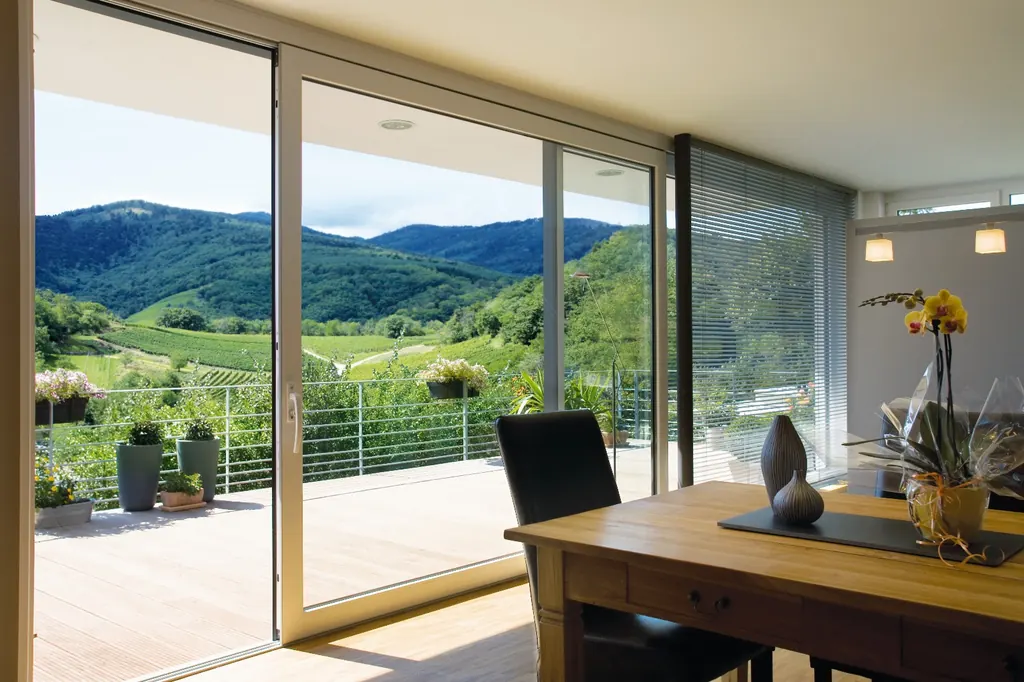 Comedor con una gran corredera de PVC blanco abierta a una terraza con vistas a un valle verde